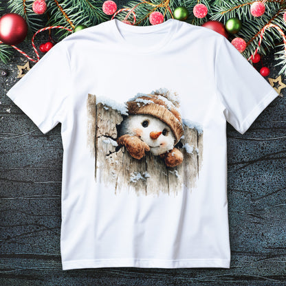 Snowman in knit beanie and mittens peeking through snowy wooden fence on a Christmas T-shirt